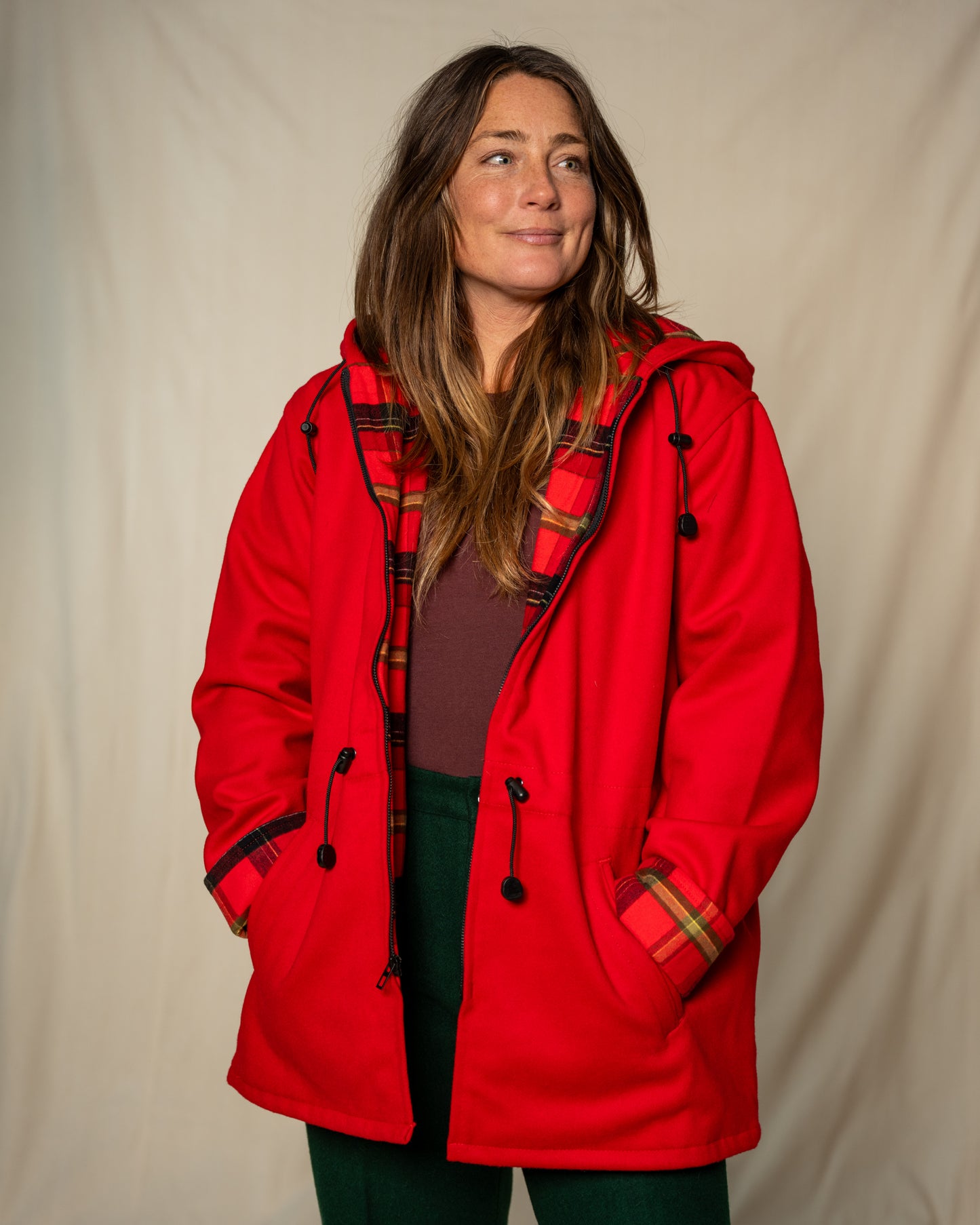 Person wearing a red coat with plaid accents against a beige background