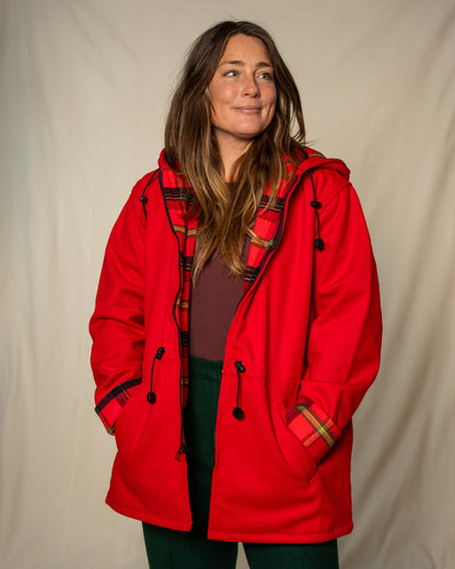 Person wearing a red coat with plaid accents against a beige background