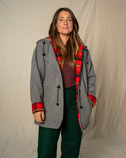 Person wearing a gray coat with red plaid lining against a plain background