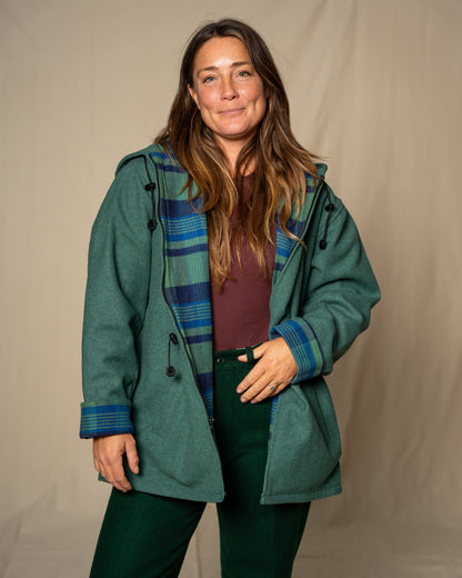 Woman wearing a green coat with plaid lining against a beige background