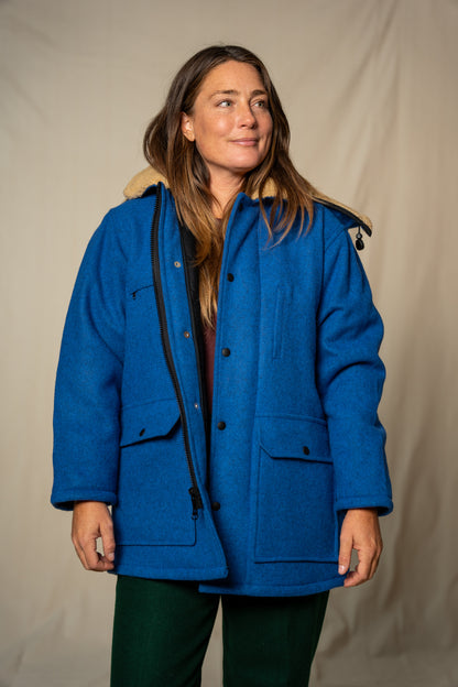 Woman wearing a blue coat with a beige hood against a plain background