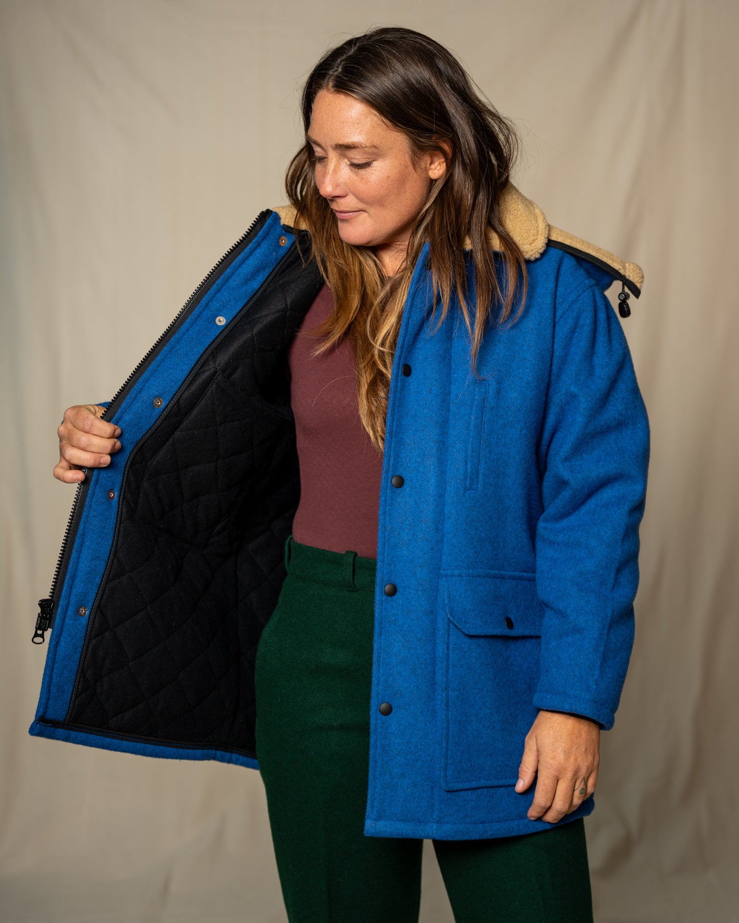 Woman wearing a blue coat with a beige hood against a plain background