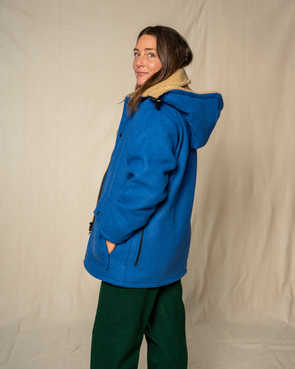 Person wearing a blue coat with a hood against a plain background