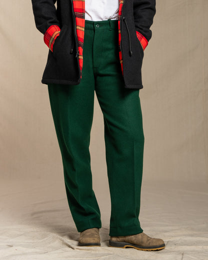 Person wearing green pants with a black coat and red plaid shirt on a beige background