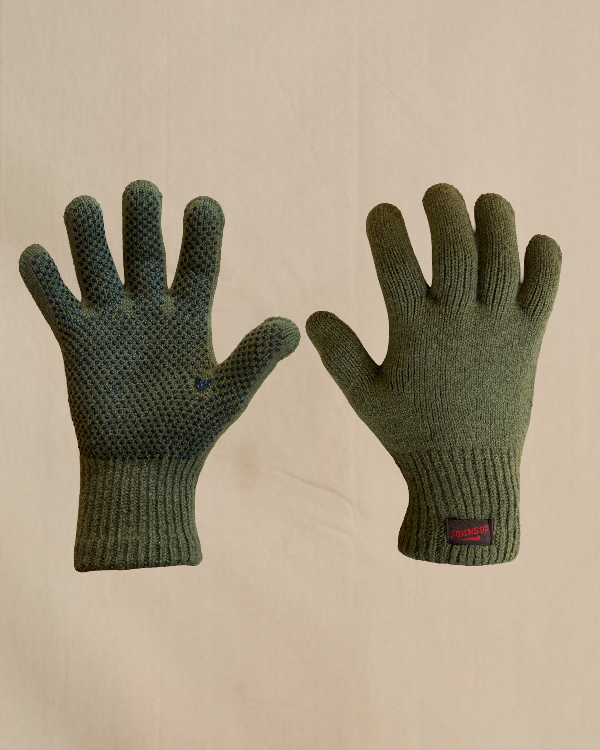 A pair of olive green merino wool knit gloves shown flat against a light beige background, with one glove displaying a textured grip pattern on the back of the hand and a small brown and red Johnson tab on the cuff.
