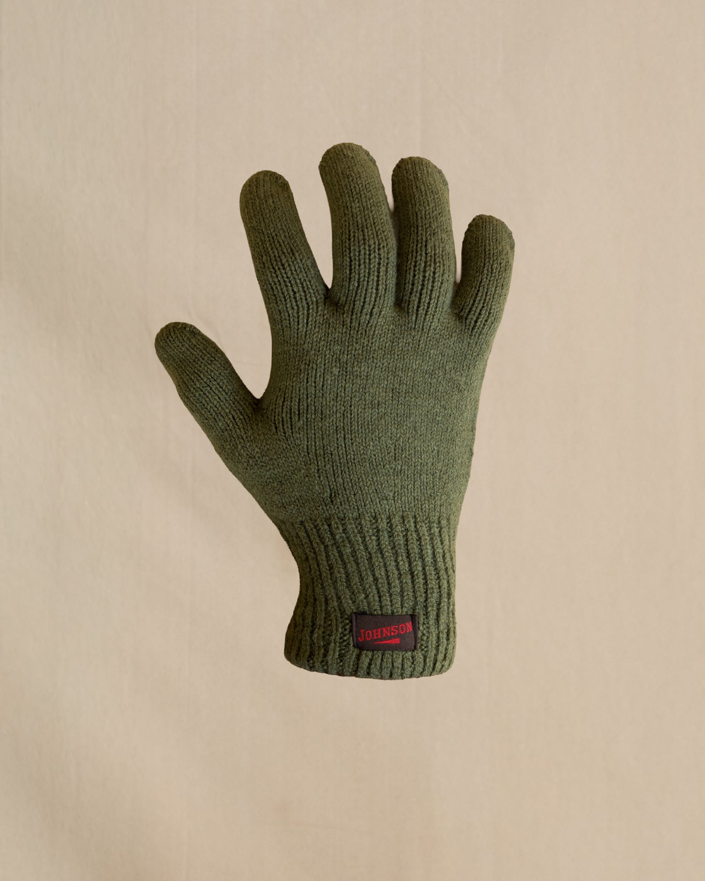 A single knit merino wool glove in olive green. The glove has a small brown and  red Johnson label on the cuff. 