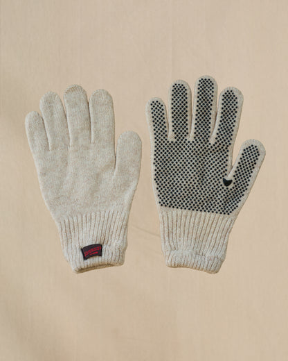 A pair of beige merino wool knit gloves shown flat against a light beige background, with one glove displaying a textured grip pattern on the back of the hand and a small brown and red Johnson tab on the cuff.
