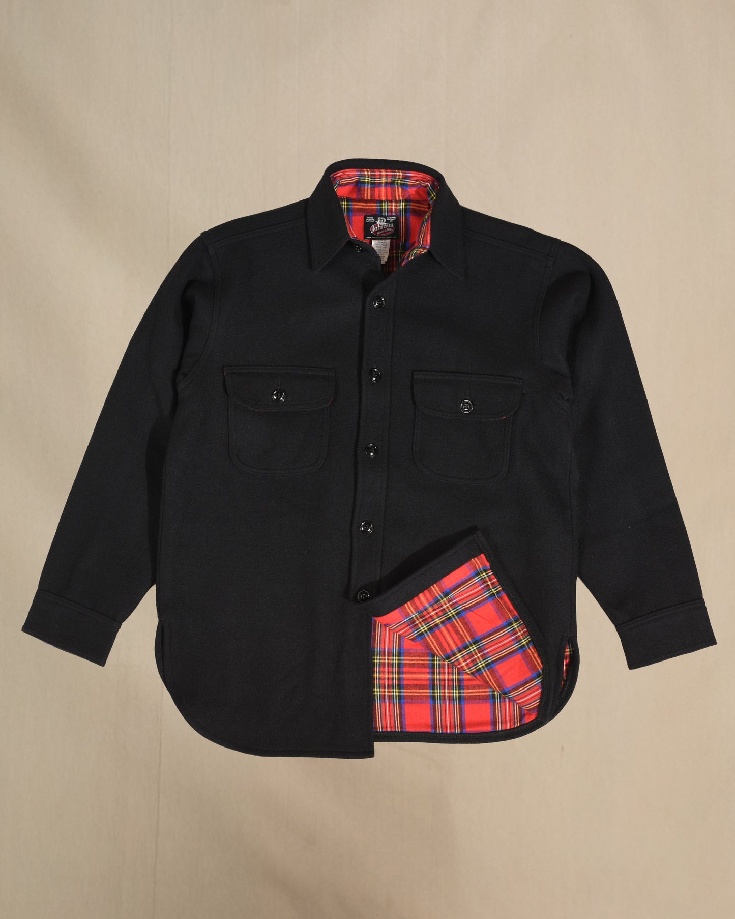 Black shirt with red plaid interior and pocket on a beige background