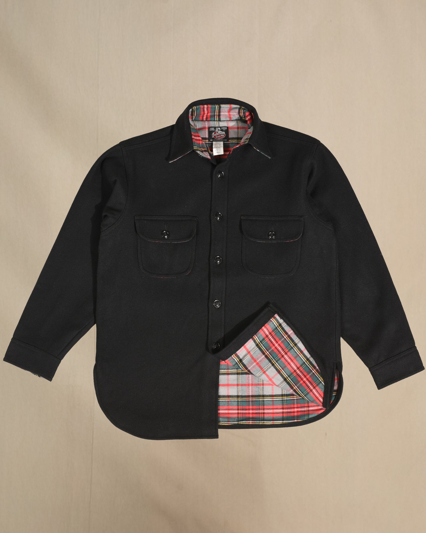 Black wool shirt with red and gray plaid interior and pocket flaps on a beige background