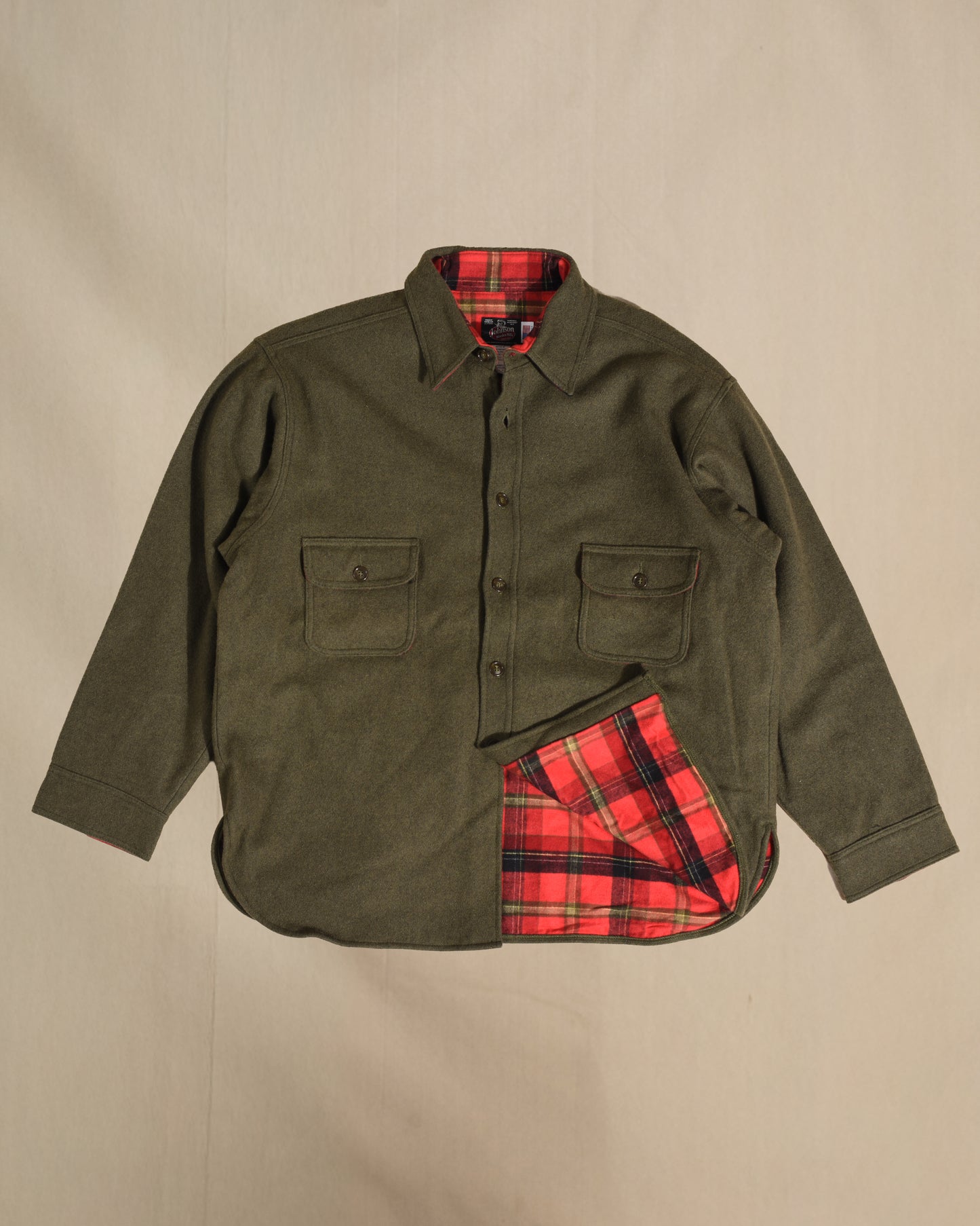 Loden wool button down shirt with red plaid lining on a beige background