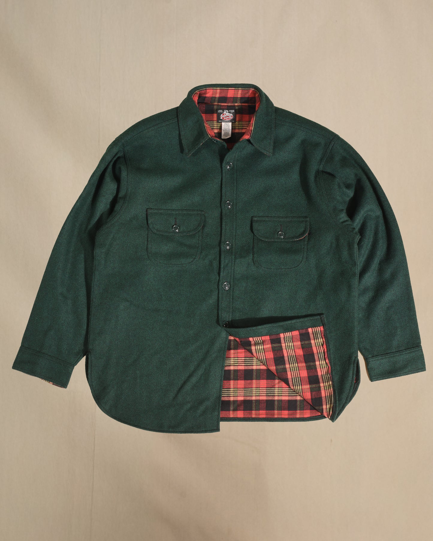 Green shirt with a red and black plaid lining on a beige background