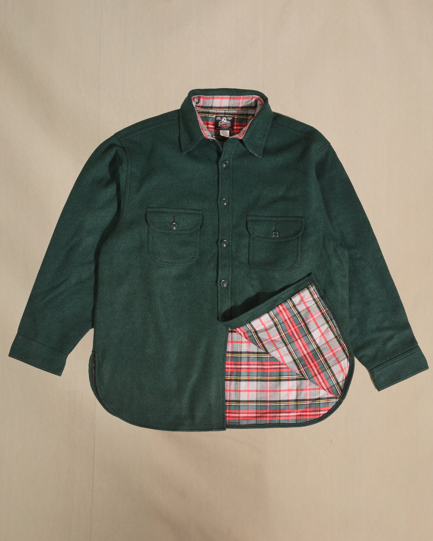 Green shirt with red and gray plaid lining on a beige background