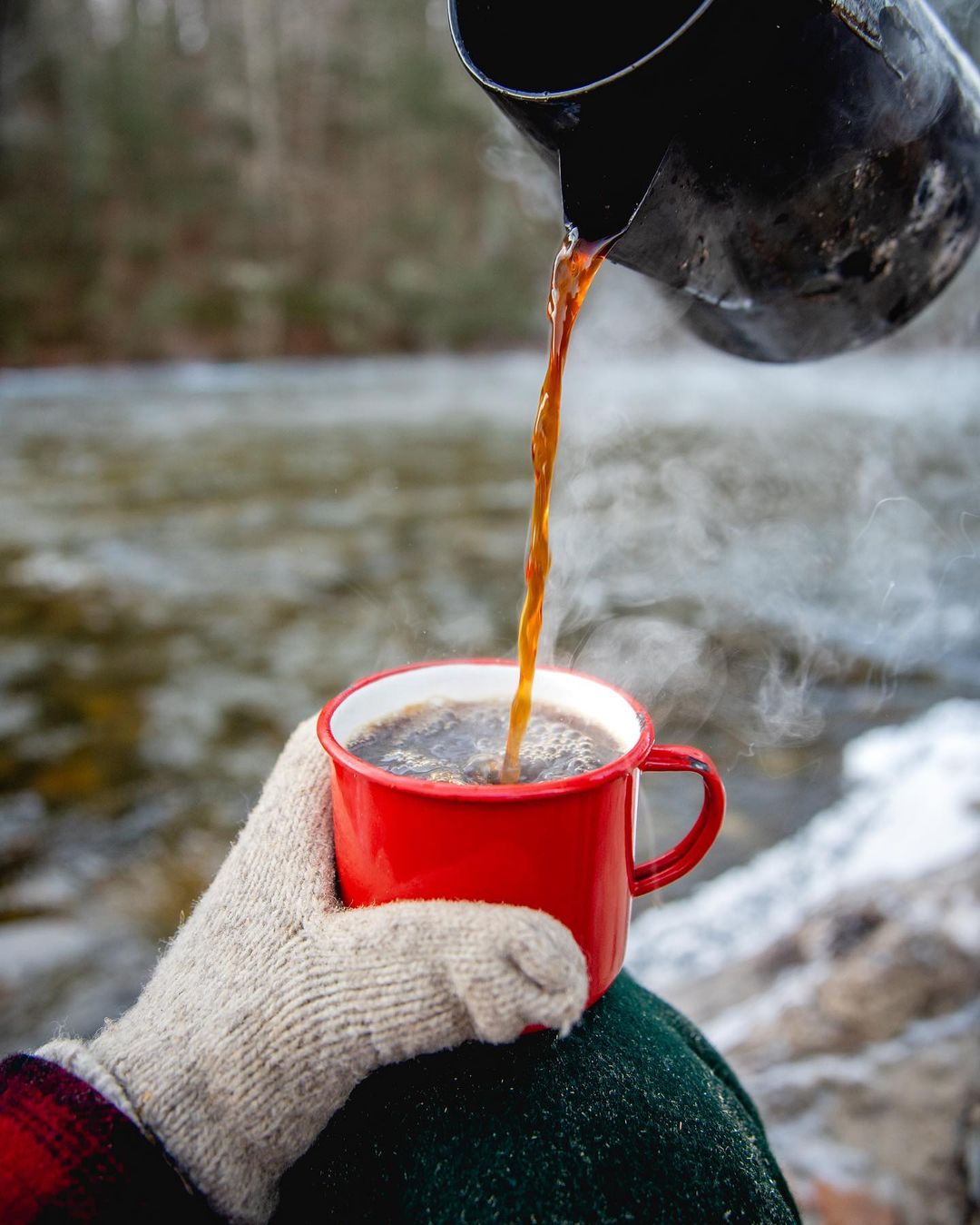 pouring hot coffee into a stormy kromer cup by a river bank