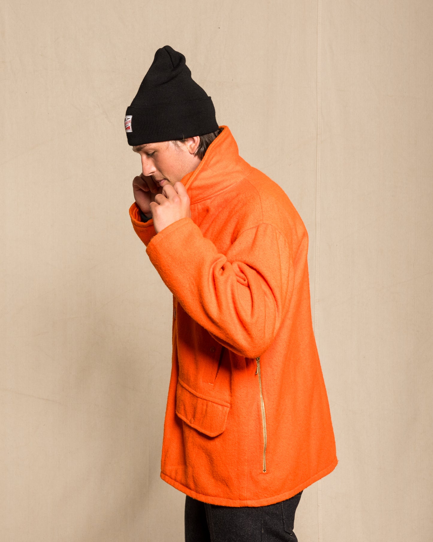 A man wearing a bright orange heavy wool vintage jacket, a black knit beanie.