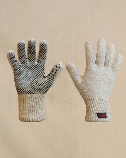 A pair of beige merino wool knit gloves shown flat against a light beige background, with one glove displaying a textured grip pattern on the back of the hand and a small brown and red Johnson tab on the cuff.