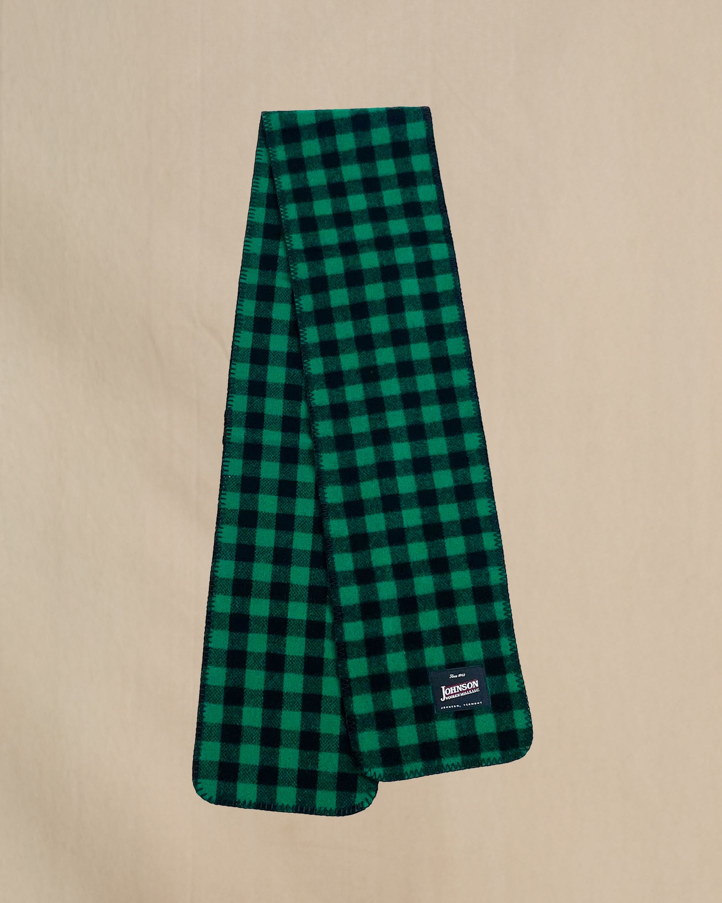 Green and black checkered scarf with a brand label on a beige background