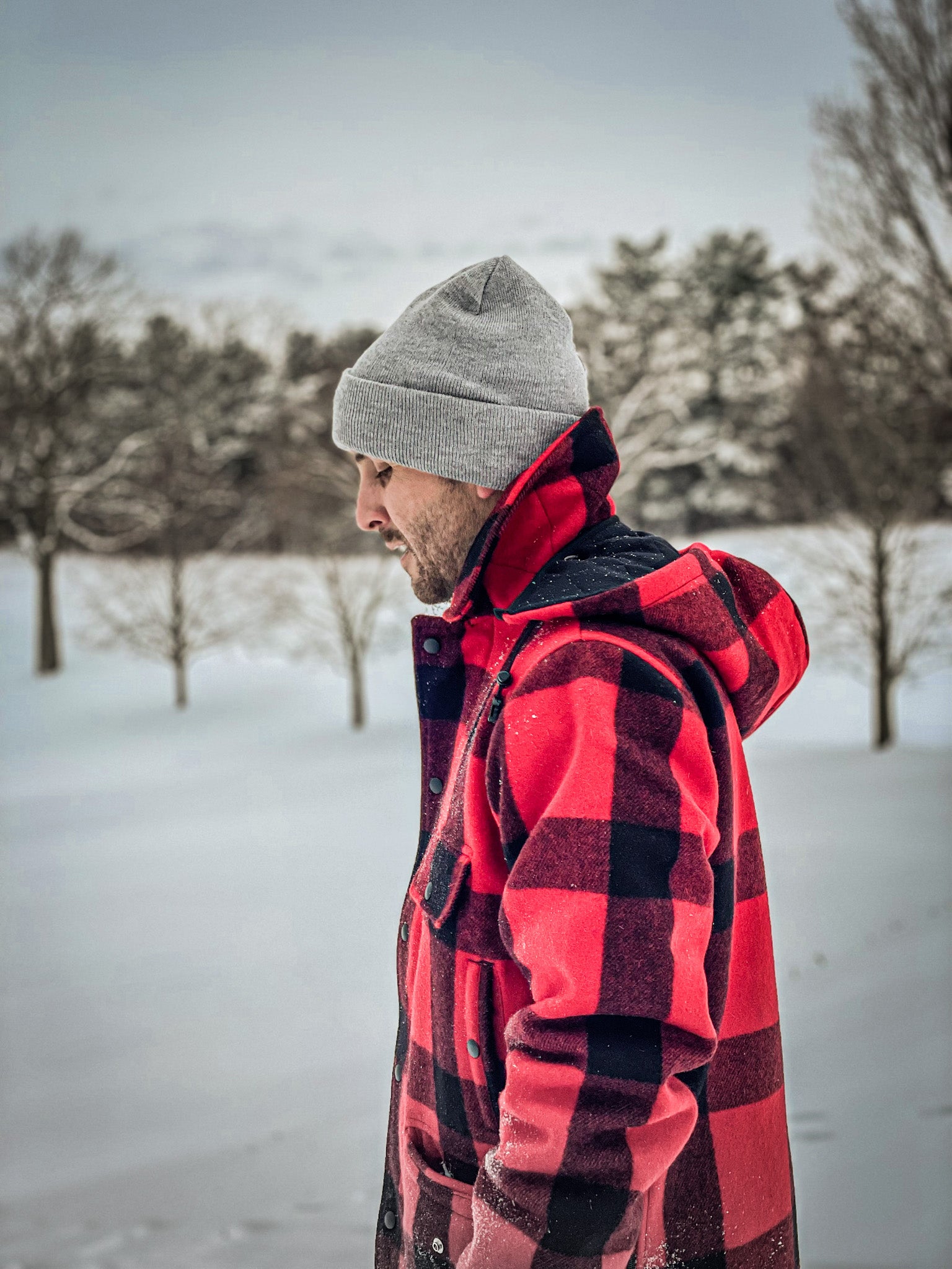 Man wearing outdoor coat with red & black squares & gray beanie in winter scene image