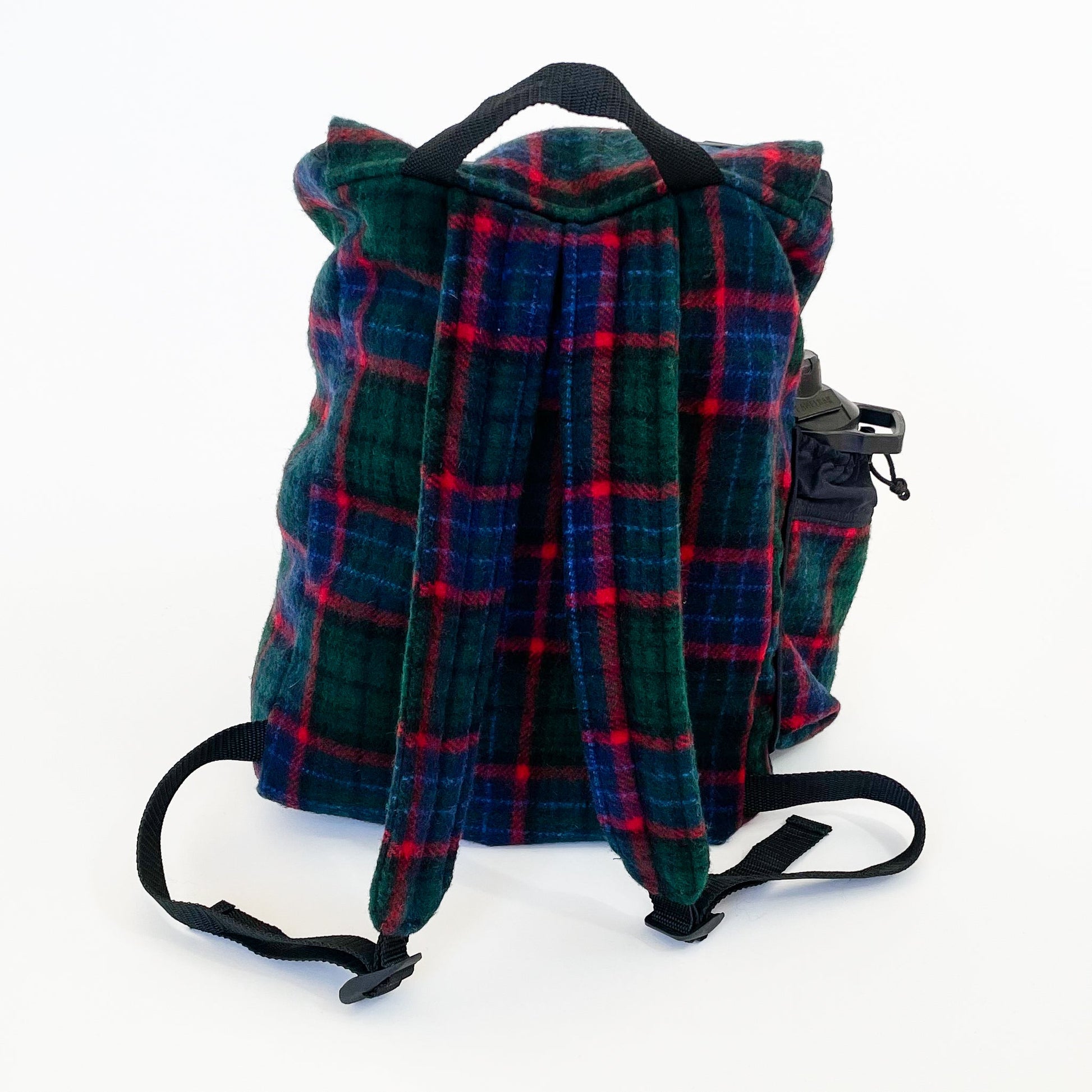 Wool back pack green and blue with red windowpane print, shown with water bottle in side pocket, back view